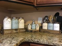 the kitchen counter has five jars on it and spoons in each jar, along with other items