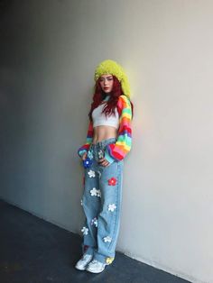 a woman with red hair is standing next to a wall wearing jeans and a rainbow sweater