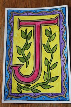 a drawing of the letter j with leaves and vines in it on a wooden surface