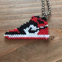 a red, white and black beaded shoe necklace on a wooden table next to a ball chain