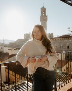 a woman standing on a balcony with her hands in her pockets and looking at the camera