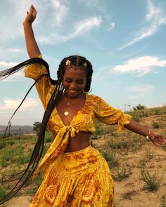 a woman in a yellow dress is dancing on the dirt road with her hair blowing in the wind