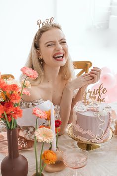 a woman sitting at a table with a cake and flowers in front of her smiling