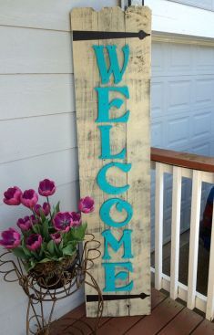 a wooden welcome sign sitting on top of a porch next to flowers and a potted plant