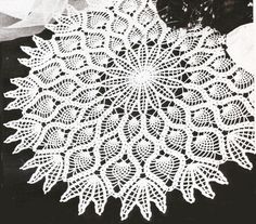 a crocheted doily with white flowers in the background on a black surface