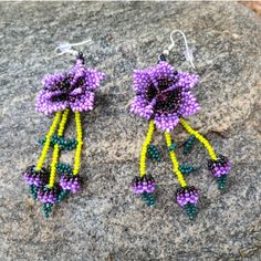 These beaded earrings come from many different families of the Wixarika(Huichol) Nation who reside in TaTeki village of San Andres, Jalisco Mexico. These pieces were purchased on pilgrimage to Wixrikuta from families who do not have the opportunity to leave and sell their art outside of the villages. Purchasing this artwork helps the locals buy food, clothing, school supplies for their children, and also candles for their prayers and offerings. For many of these artisans, this work is their only Traditional Handmade Flower Earrings, Traditional Handmade Flower Earrings For Festivals, Handmade Traditional Flower Earrings For Festivals, Purple Traditional Earrings For Gift, Traditional Handmade Dangle Flower Earrings, Traditional Colorful Beaded Flower Earrings For Festivals, Traditional Green Jewelry With Bead Caps, Traditional Multicolor Flower Earrings With Dangling Beads, Traditional Beaded Flower Earrings For Festival