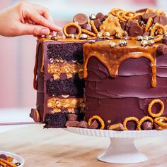 someone is cutting into a chocolate cake with pretzels and caramel on top