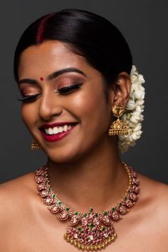 a woman wearing a necklace and earrings with flowers in her hair, smiling at the camera