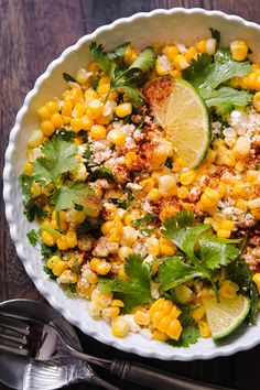 a white bowl filled with corn and cilantro on top of a wooden table