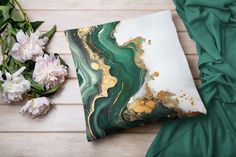 a green and gold pillow sitting on top of a wooden floor next to white flowers