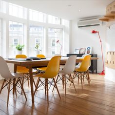 a dining room table with yellow chairs in front of large windows and wood flooring