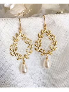 a pair of gold earrings with pearls hanging from the ends of them, on top of a white cloth