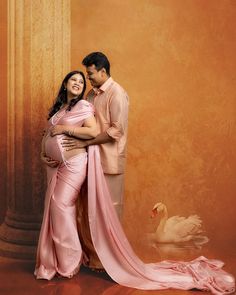 a pregnant woman in a pink dress standing next to a man with a swan behind her