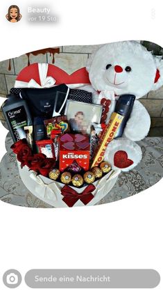 a white teddy bear sitting next to a valentine's day gift basket filled with chocolates and candy