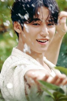 a young man is posing for a photo in front of some trees and water droplets