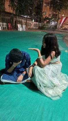 two people sitting on the ground in front of a swimming pool