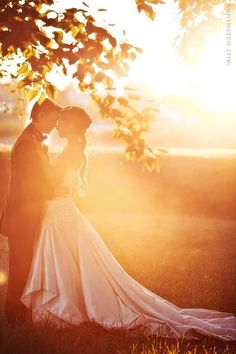 the bride and groom are posing for their wedding photo in front of the sun setting