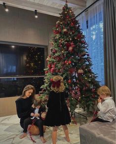 two women and a child sitting in front of a christmas tree