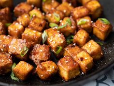 tofu with sesame seeds and seasoning in a black bowl on a tablecloth