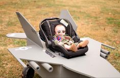 a baby sitting in a car seat on top of a plane shaped table with wheels