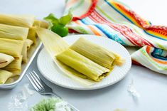 corn on the cob is sitting next to a white plate with some green leaves