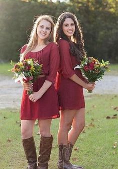 two women in red dresses holding flowers and standing next to each other on the grass