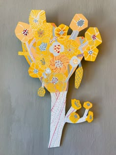 an origami flower arrangement is displayed on a gray wall with yellow flowers in it