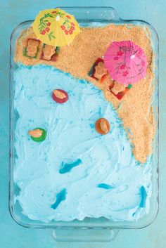 a cake with blue frosting and two umbrellas on the beach in front of it