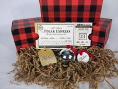 a red and black plaid box with ornaments in it on a white surface next to a card that says polar express