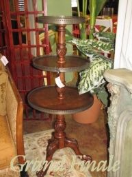 three tiered cake stand sitting on top of a table next to a chair and potted plant