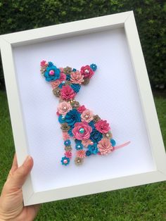 a hand holding up a framed letter made out of flowers