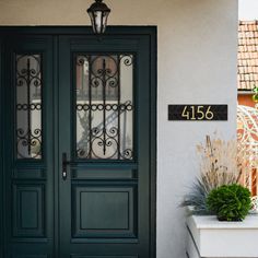 the front door to a house with two potted plants and a number plate on it