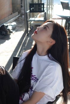 a woman with long hair sitting on a bench looking up at the sky and sun