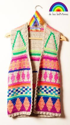 a crocheted vest hanging on a wooden hanger next to a white wall