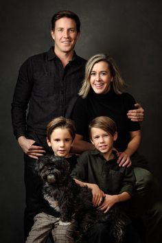 a man and two boys with their dog posing for a family photo in front of a black background