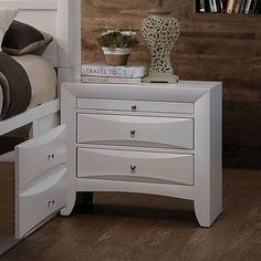 a white night stand with three drawers and a vase on top of it next to a bed