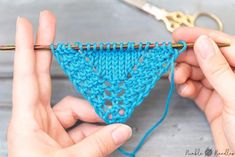 two hands are holding a crochet triangle with yarn on it and one hand is knitting