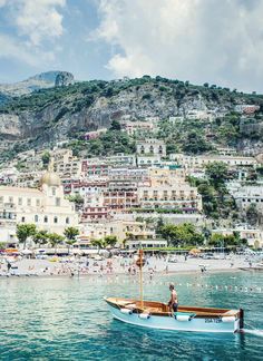 a boat floating on top of the ocean next to a beach covered in people and buildings