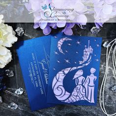 two blue cards sitting on top of a table next to some flowers and beads,