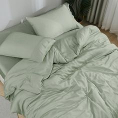 an unmade bed with green sheets and pillows