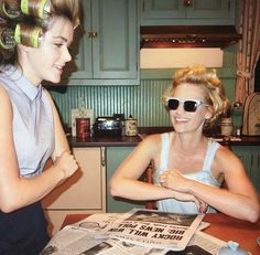 two women sitting at a table with newspapers in front of them and one is wearing sunglasses