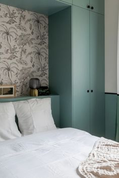 a bed with white sheets and pillows in a bedroom next to a green cupboards