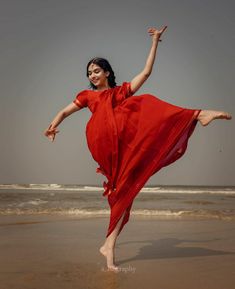 a woman in a red dress is dancing on the beach with her legs spread out