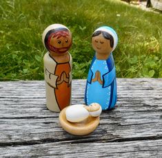 two small wooden dolls sitting on top of a wooden table next to each other in front of green grass