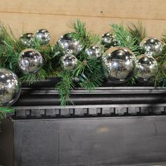 silver balls and pine branches on top of a fireplace mantel