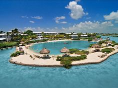 an island in the middle of water with thatched umbrellas on it's sides