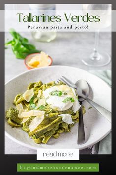 a white plate topped with pasta and pesto next to a glass of red wine