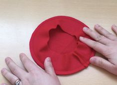 two hands are holding onto a red hat on a wooden table with one hand reaching for the other