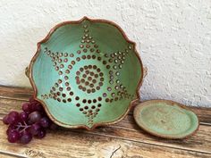 a green bowl sitting on top of a wooden table next to a bunch of grapes