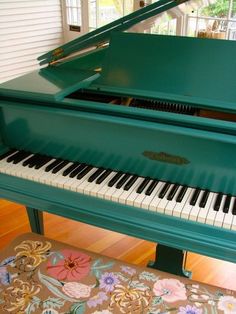 a green piano sitting on top of a hard wood floor next to a rug and window